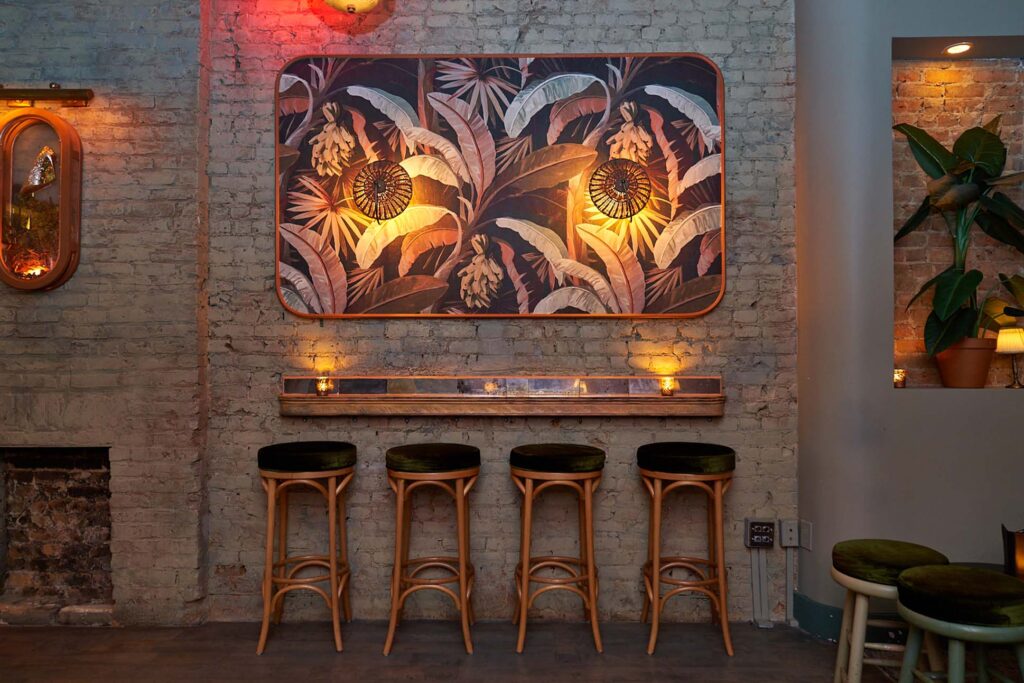 Speakeasy bar with moody lighting and stools against a wall.