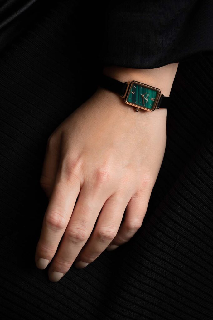 Photo of a woman's hand with an emerald plated luxury watch.