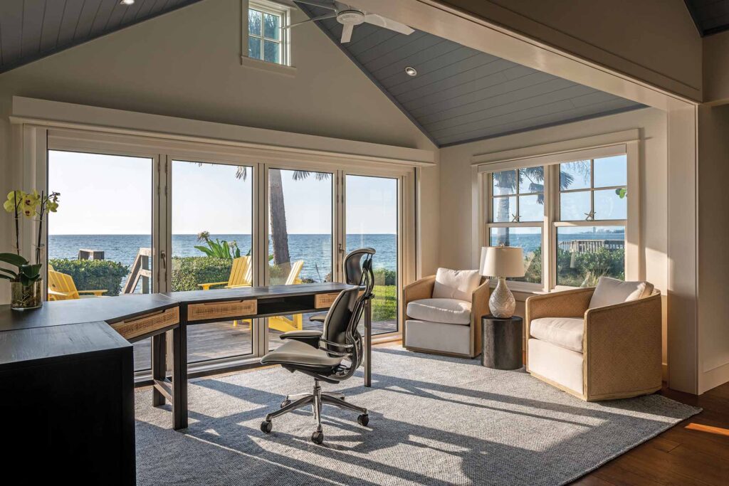 a room with a desk and chairs and a table with a view of the ocean
